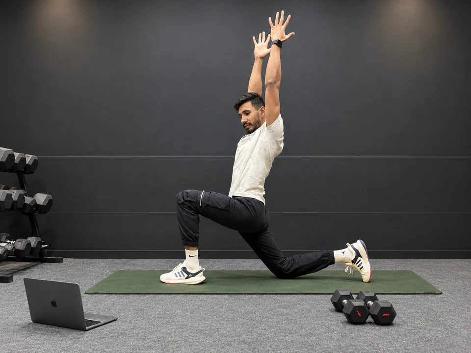 Maddy demonstrating a kneeling mobility movement beside his laptop and exercise mat.
